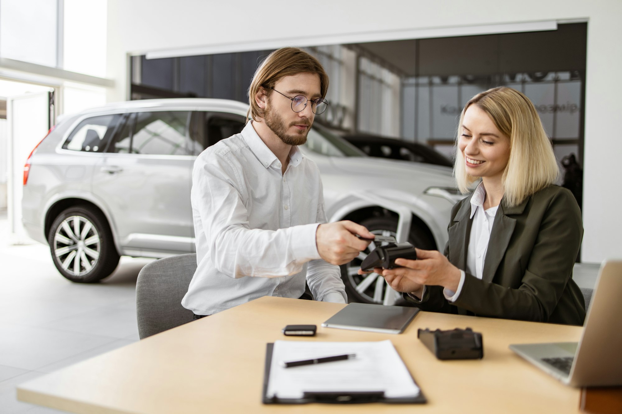 Happy man paying with electronic credit card at terminal for purchase of car.